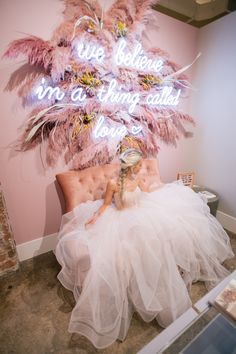 a woman in a white dress sitting on a chair with pink feathers hanging from it