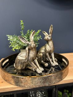 two bronze rabbits sitting on top of a metal tray next to a potted plant