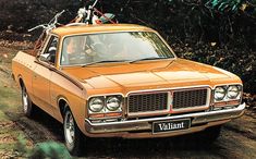 an orange car driving down a dirt road with bicycles on the top of it's roof