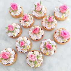 twelve cupcakes decorated with pink roses and white frosting on a marble surface