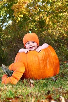 a baby in a pumpkin costume sitting on the ground with its arms around it's head