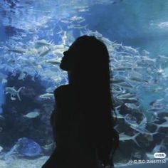 a woman standing in front of an aquarium looking at fish