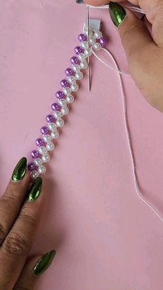 two hands are working on an object with pearls and green nail polishing scissors next to it