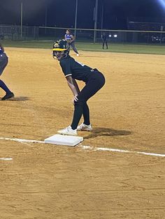 two softball players are on the field during a game at night with lights in the background