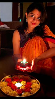 a woman holding a lit candle in front of a plate with flowers and petals on it