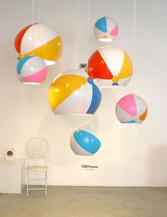 an assortment of colorful beach balls hanging from the ceiling in a room with white walls