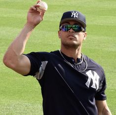 a man holding a baseball in his right hand and wearing sunglasses on top of it