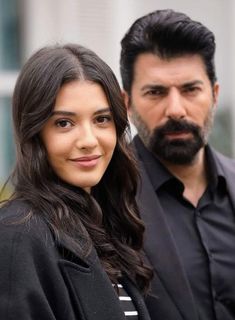 a man and woman standing next to each other in front of a building with one person looking at the camera