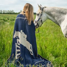 a woman wrapped in a blanket sitting next to a white horse on a lush green field