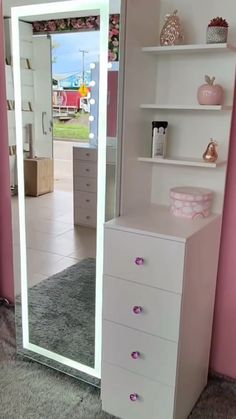 a white dresser sitting in front of a mirror on top of a floor next to a pink wall