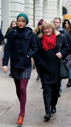 several people walking down the street with one woman wearing a red scarf and black coat