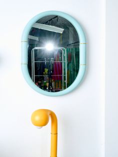 a round mirror hanging on the wall above a yellow lamp