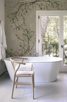 a white bath tub sitting under a window next to a wooden chair and towel rack