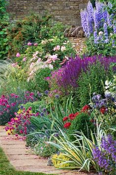 a garden filled with lots of flowers next to a brick wall and grass covered walkway