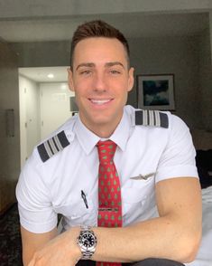 a man wearing a pilot's shirt and tie sitting on a bed in a hotel room