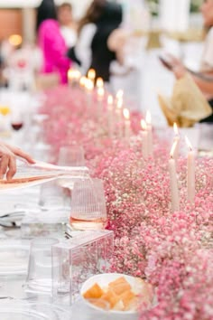 people are sitting at a long table with pink flowers and candles