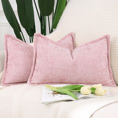 two pink pillows sitting on top of a white couch next to a green potted plant