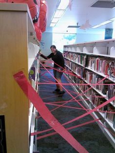 a man standing in front of a book shelf filled with lots of books next to red tape