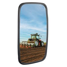 a rear view mirror showing a tractor in the middle of a field with blue sky and clouds