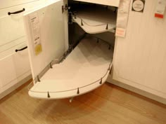 an open cabinet in the middle of a kitchen with white cupboards and wood flooring