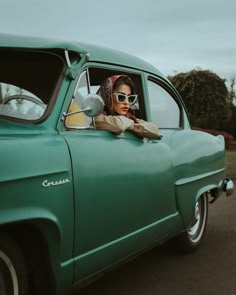 a woman wearing sunglasses sitting in the driver's seat of an old green car