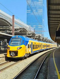 a yellow and blue train traveling down tracks next to a tall building in the background