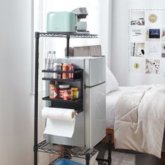 a small room with a bed, refrigerator and various items on the shelf in front of it