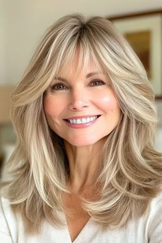 Save this pin for the best medium-length hairstyles for women over 50 with bangs. Feathered layers shape the face gently while adding volume to the hair. The light, wispy bangs create an airy, wispy effect, blending seamlessly with the rest of the hair. Medium Length Hair With Layers And Wispy Bangs, Medium Layered Hair With Bangs Over 40, Bangs Feathered, Feathered Layered Hairstyles, Light Wispy Bangs, Medium Length Blonde Hair With Layers Side Bangs, Long Layered Grey Hair With Bangs