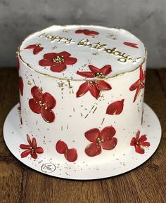 a white cake with red flowers on it sitting on top of a wooden table next to a wall