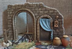 a miniature house made out of clay with a blue curtain on the door and two vases next to it