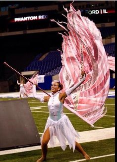 a cheerleader is performing on the field at a football game with her pink and white flag