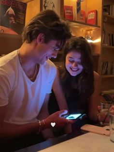 a man and woman sitting at a table looking at a cell phone together, both smiling