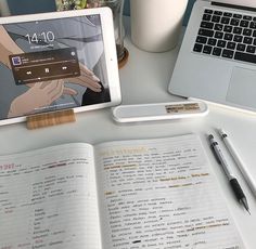 an open book sitting on top of a desk next to a laptop computer and pen