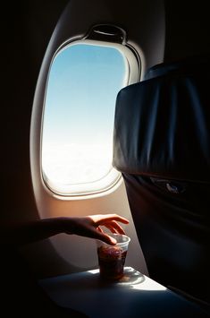 a person reaching out the window of an airplane to touch a cup with their hand