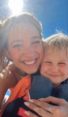 a woman holding a boy in her arms and smiling at the camera with sun shining on him