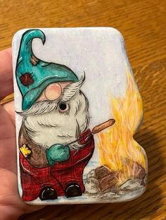 a hand holding a small glass magnet with a painting of a gnome on it's face