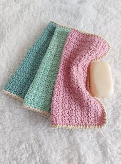 two crocheted washcloths and a soap dish on a white towel with a pink, blue, and green stripe