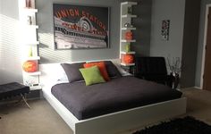 a bedroom with gray walls and orange pillows on the bed, white shelve bookshelves