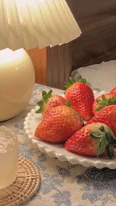 strawberries in a bowl on a table next to a glass of milk and a lamp