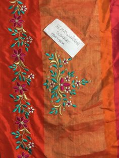 an orange and red cloth with embroidered flowers on it, next to a white tag