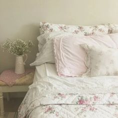 a white bed topped with lots of pillows next to a vase filled with baby's breath