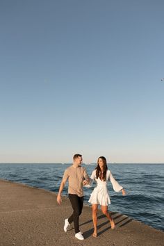 a man and woman are walking along the water