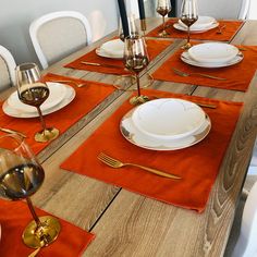 the table is set with place settings and wine glasses on it, along with orange napkins