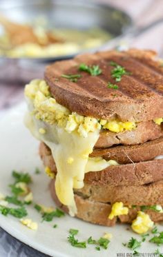 a stack of four breakfast sandwiches on a plate with eggs, cheese and chives