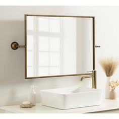 a white sink sitting under a bathroom mirror next to a vase with dry grass in it