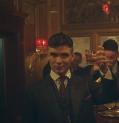 a man in a suit holding up a glass filled with liquid while standing next to other men