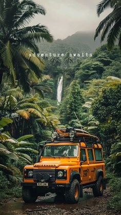 an orange jeep driving down a dirt road in front of lush green trees and a waterfall