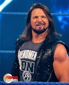 a man with long hair wearing a leather vest and smiling at the camera while standing in front of a blue background