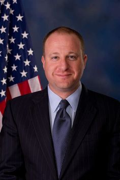 a man wearing a suit and tie in front of an american flag