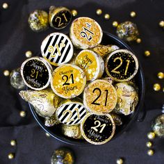 a bowl filled with lots of gold and black birthday cake pops on top of a table